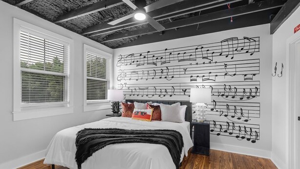 A bedroom with a bed, white walls, a ceiling with exposed beams, and a wall with musical notes. - Elegant 1BR Condo at The Sanctuary Near Local Attractions (Biloxi)