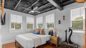 A bedroom with a bed, wooden nightstands, a suitcase, and a ceiling fan. - The Sanctuary Spacious 1BR Condo. Stay in Comfort! (Biloxi)