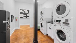 Une buanderie moderne avec des lave-linge et des sèche-linge superposés, un réfrigérateur noir et un plancher en bois.