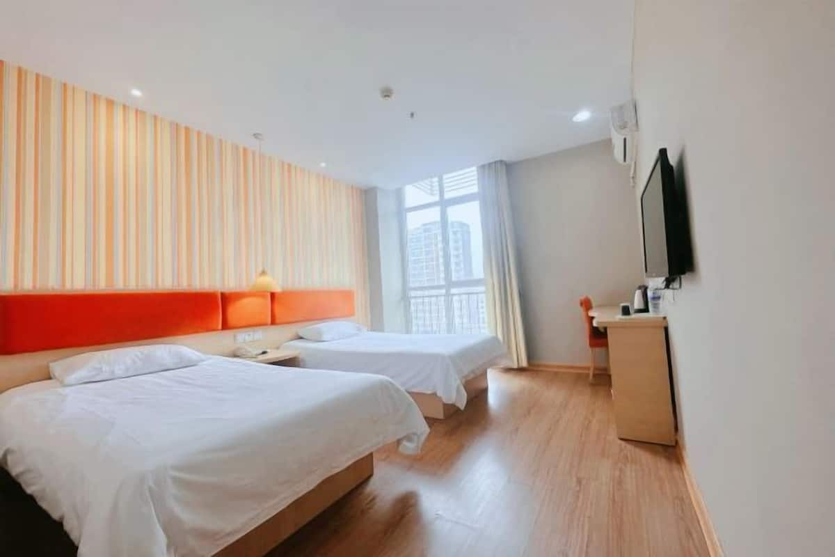 A hotel room with two beds, a wooden floor, a TV on the wall, and a window with curtains.