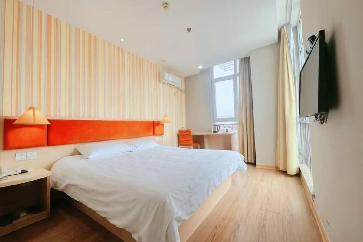A hotel room with a bed, a desk, a chair, a TV, and a window.
