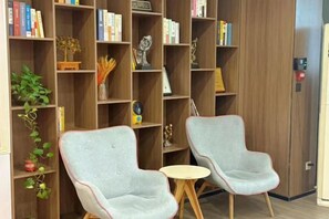 Una habitación con dos sillones, una mesita redonda y una estantería llena de libros y objetos decorativos.