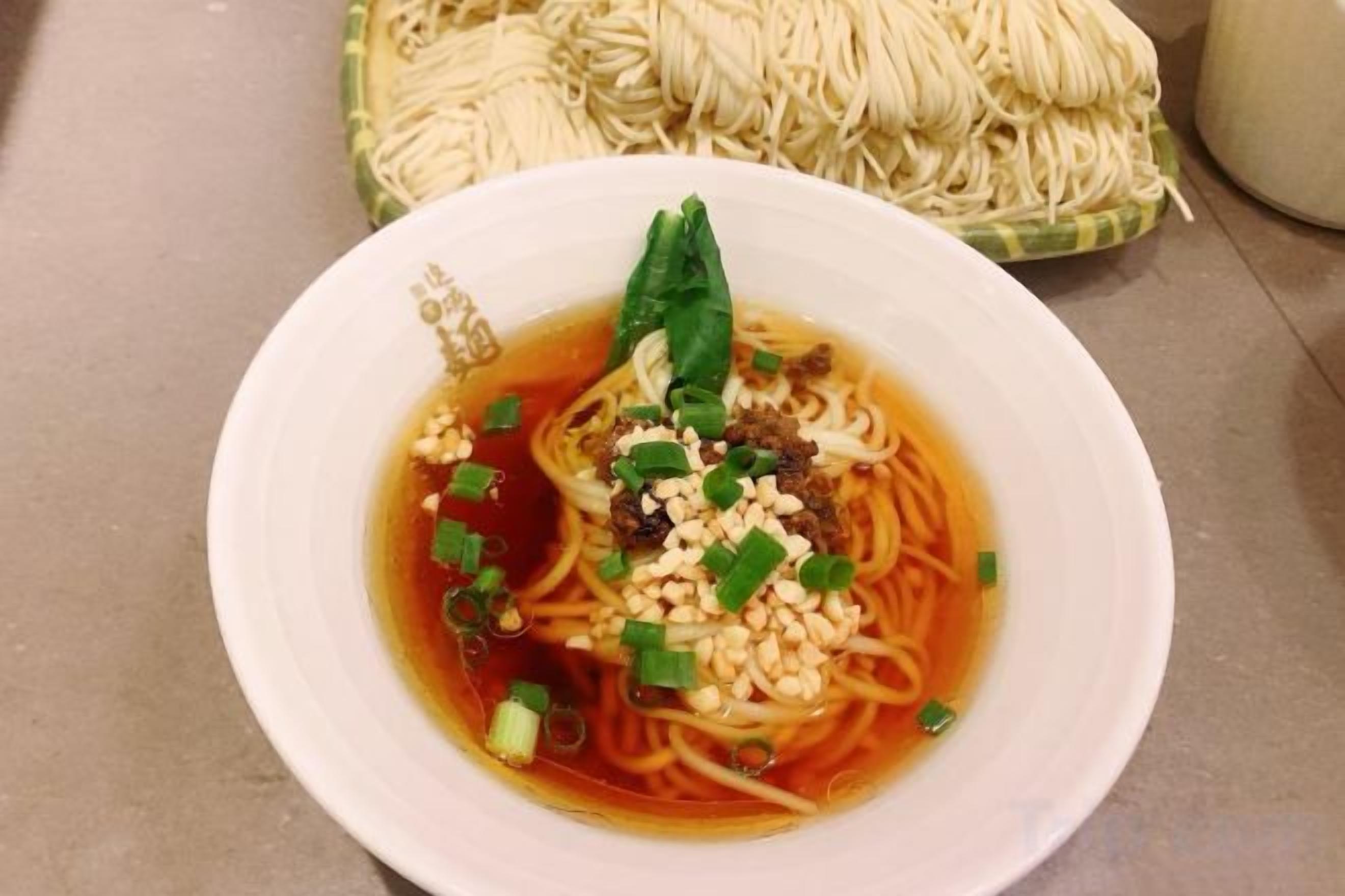 Eine Schüssel Ramen mit Nudeln, Brühe, Frühlingszwiebeln und einer Garnitur.