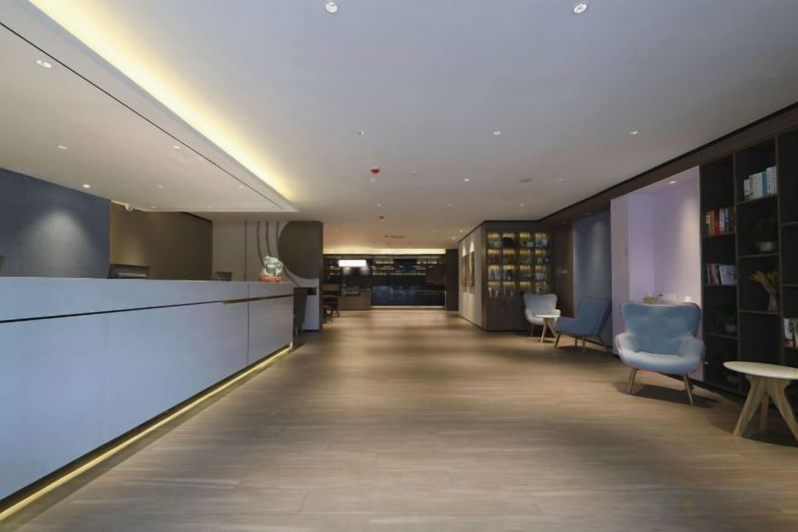 A modern hotel lobby with a reception desk, seating area, and a bookshelf.