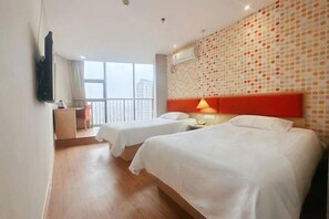 Habitación de hotel con dos camas, un escritorio, un televisor y una ventana con vista a edificios.