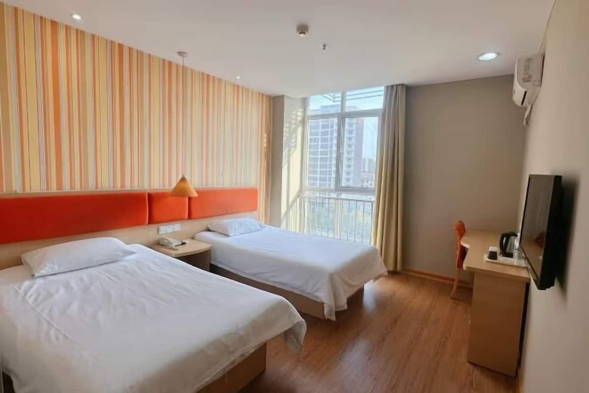 A hotel room with two beds, a desk, a chair, a TV, and a window with a view of buildings.