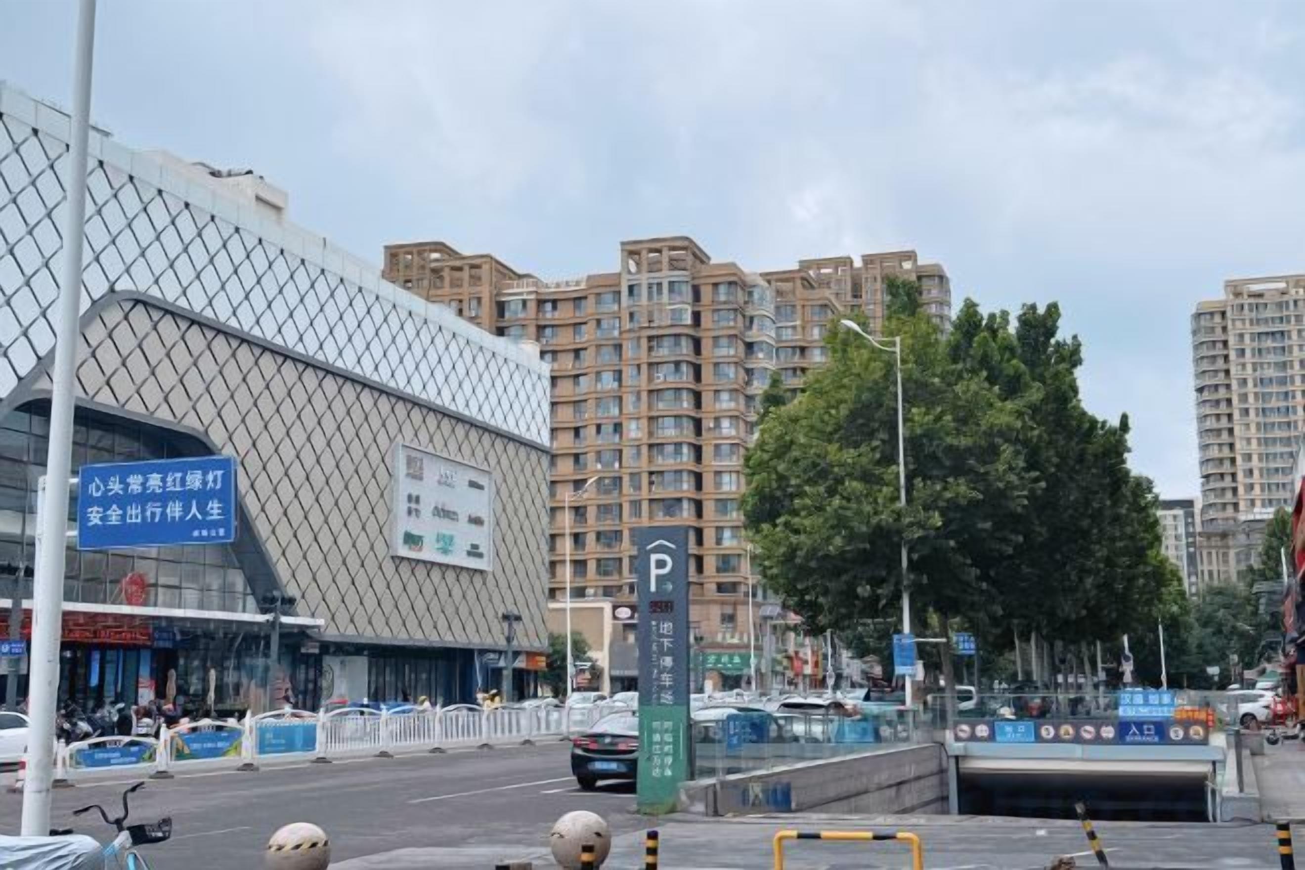 A modern building with a unique geometric facade, a parking sign, and a tree-lined street.