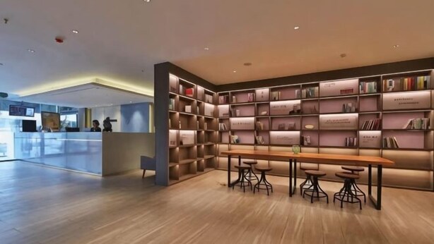A modern library with bookshelves, a wooden table, and bar stools. - Homeinn Hotel (Qingdao Zhengyang Middle Road Wanda Plaza) (Qingdao)