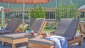 Zona de piscina con sillas de descanso, una mesa con bebidas y una sombrilla.