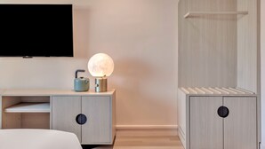 Un dormitorio moderno con cama, mesita de noche con lámpara, televisor montado en la pared y armario con espejo.