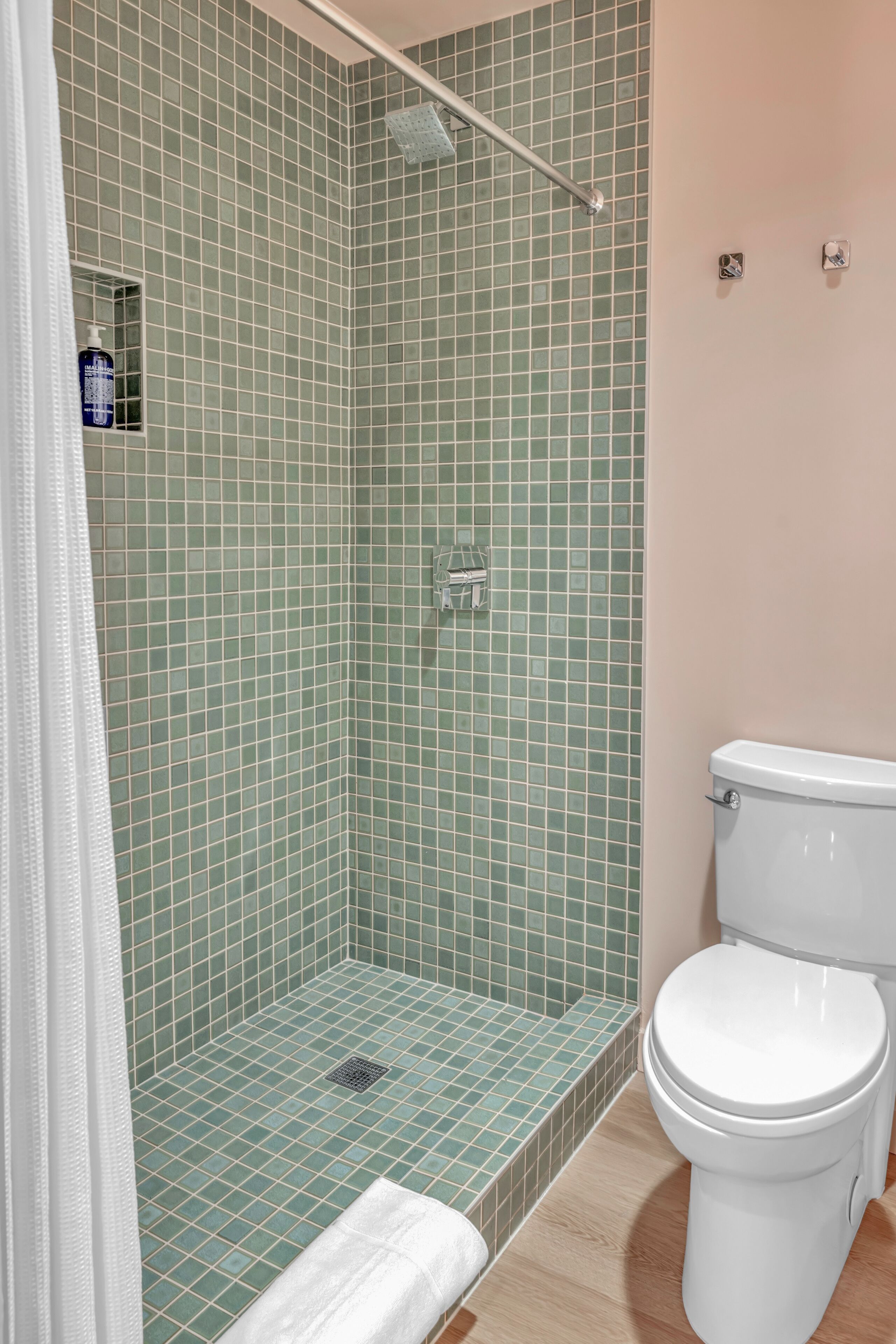 Een badkamer met groen betegelde wanden, een wit toilet en een douchegedeelte.