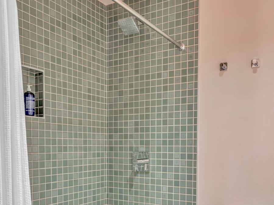 Un baño con paredes de azulejos verdes, un inodoro blanco y una zona de ducha.