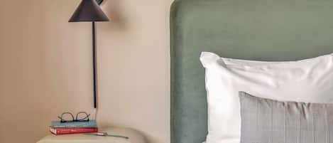 A neatly arranged bedroom with a bed, a bedside table with books and glasses, and a floor lamp.