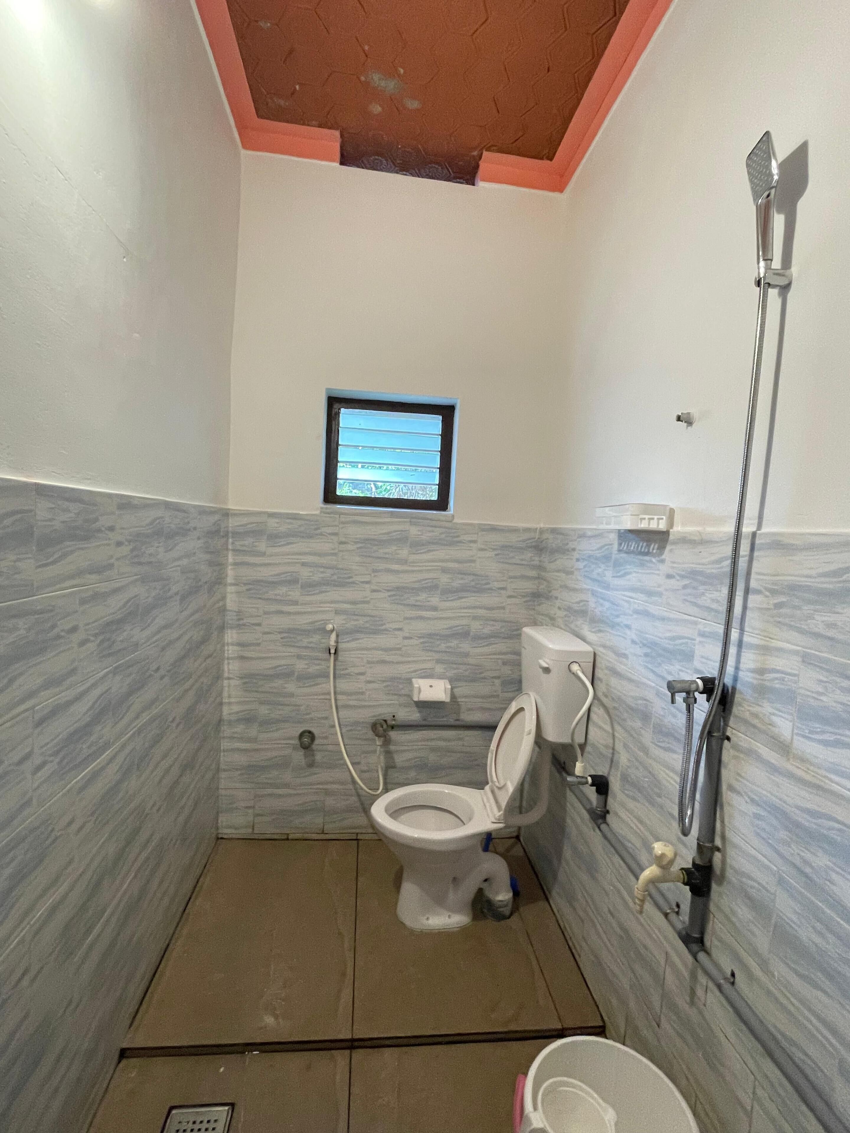 A small bathroom with a toilet, a window, and a shower.