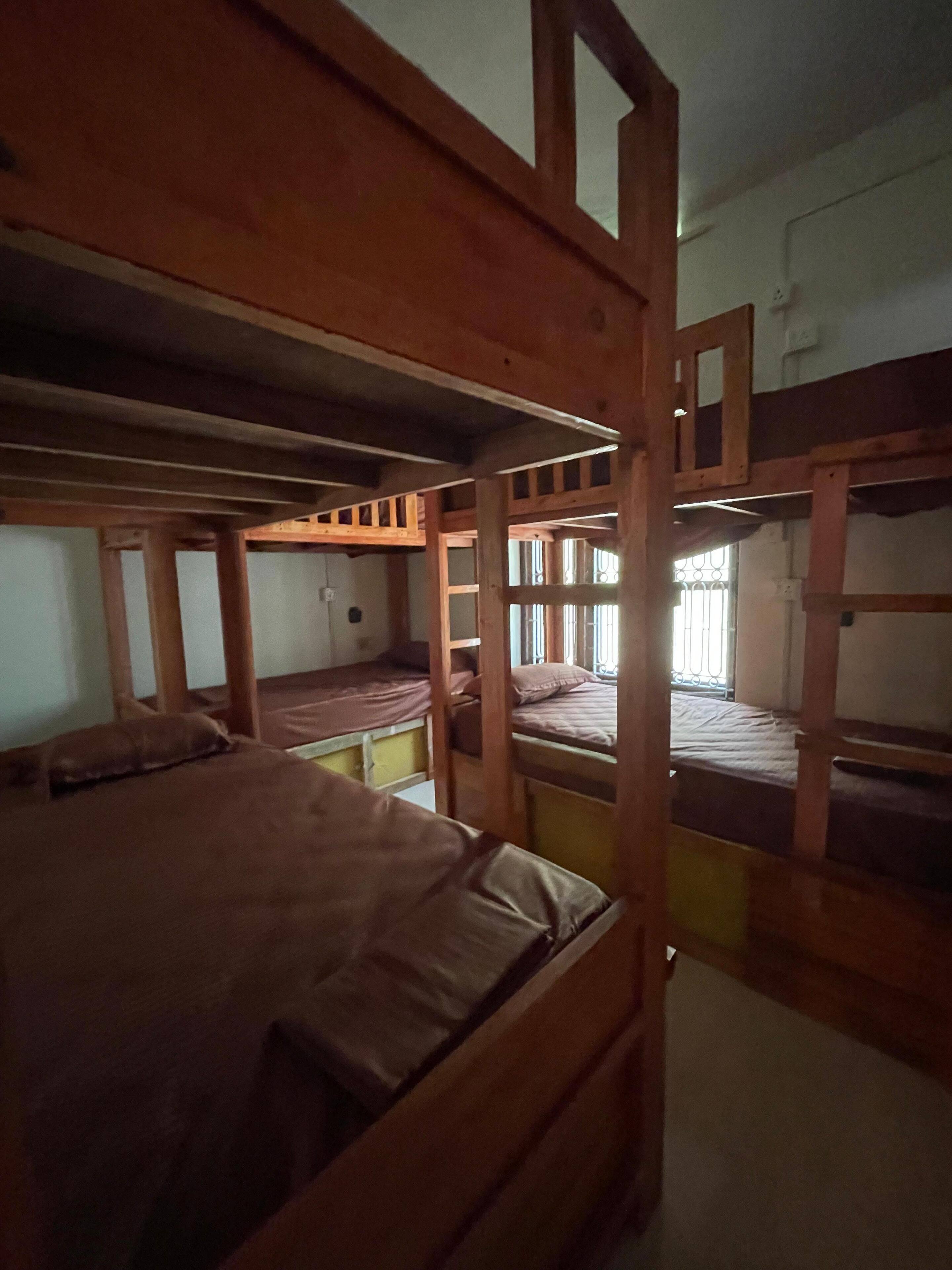 A dormitory room with bunk beds, wooden beams, and a window with bars.