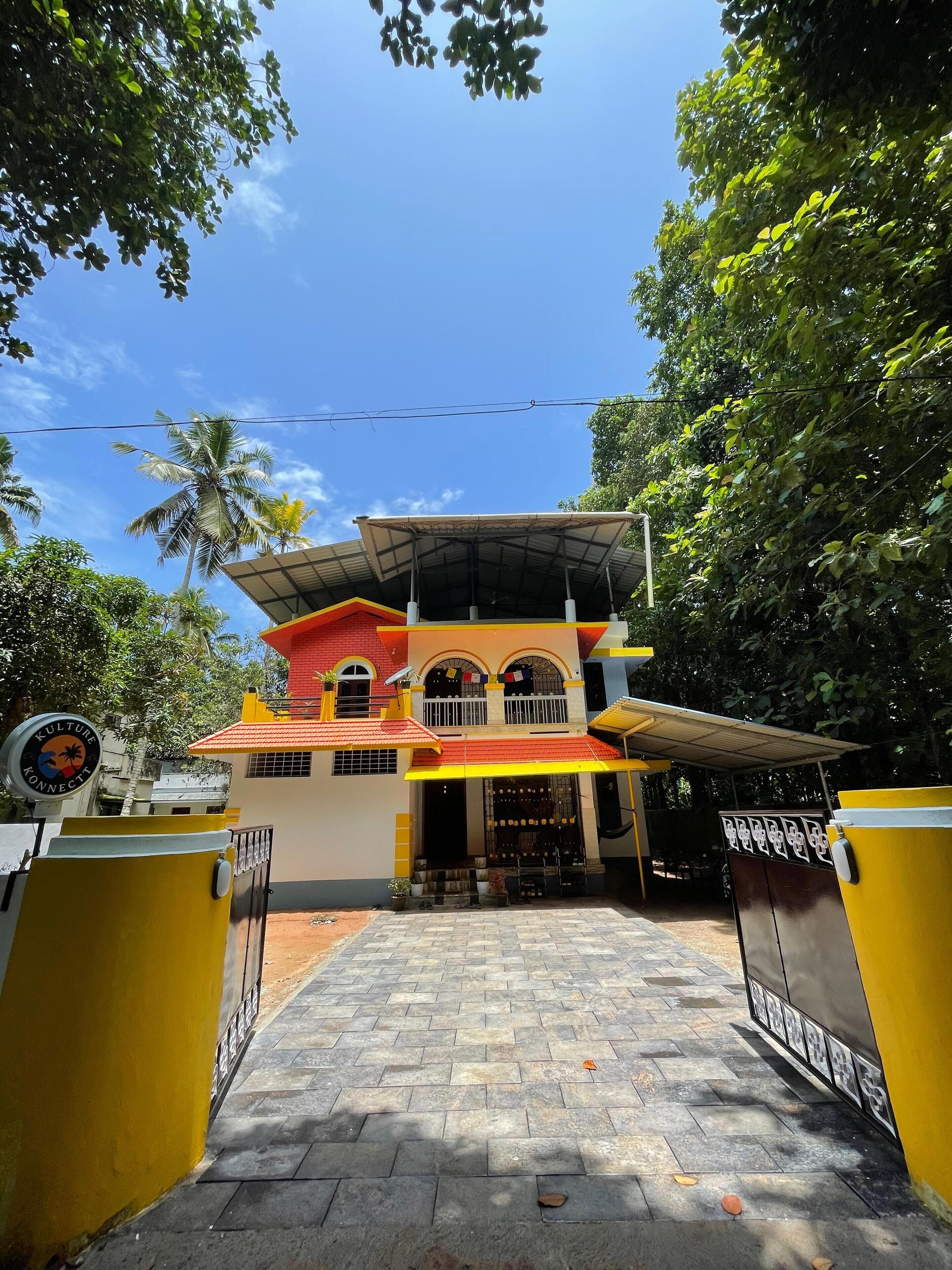Un bâtiment à deux étages avec une façade rouge et jaune, une entrée couverte et une allée pavée.