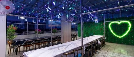 A restaurant with a long table, chairs, and a green wall with a neon heart.