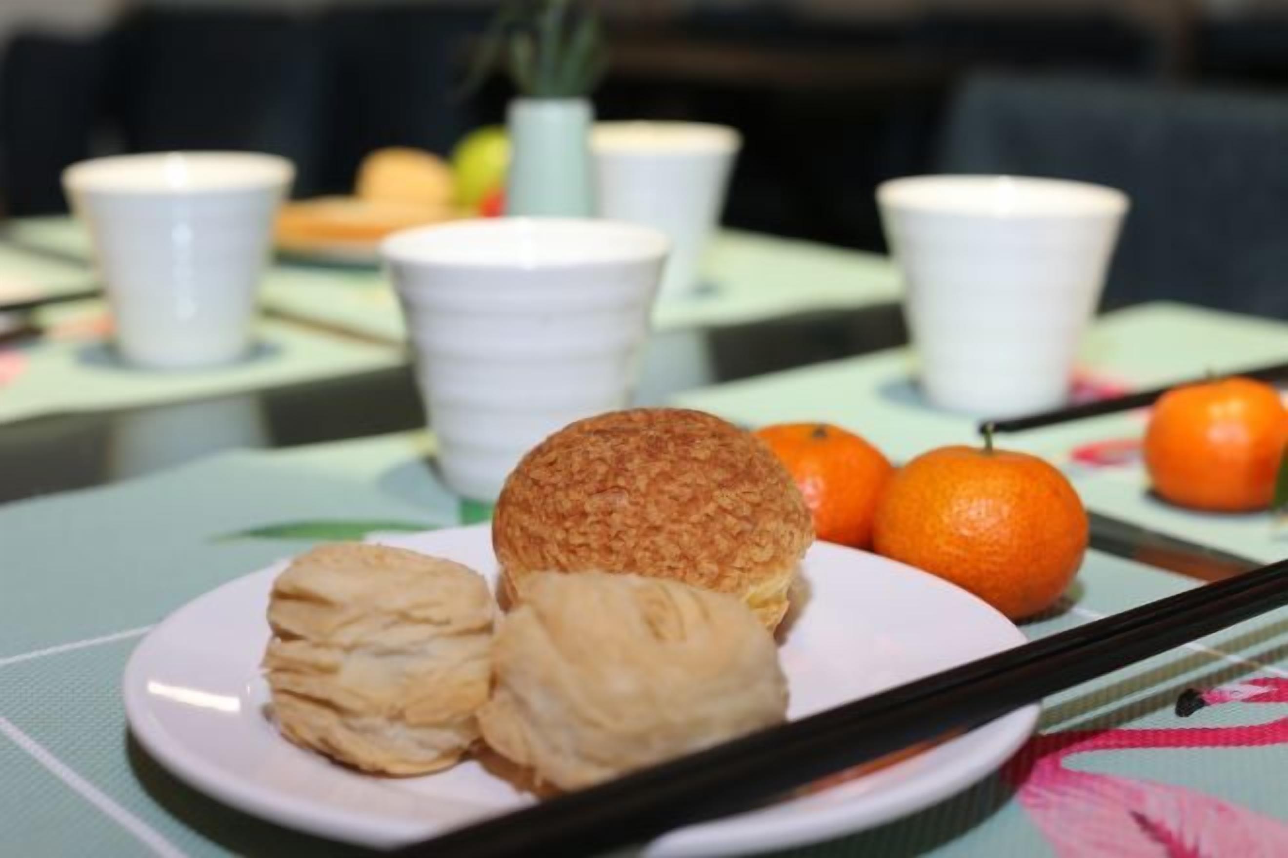 Un plato con pasteles y naranjas sobre una mesa con tazas blancas y un florero.