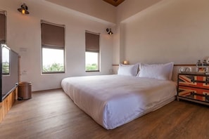 Ein Schlafzimmer mit einem großen Bett, zwei Fenstern, einem Fernseher und einem Holzboden.