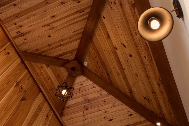 Un plafond en bois avec un luminaire suspendu et une structure de poutres apparentes.