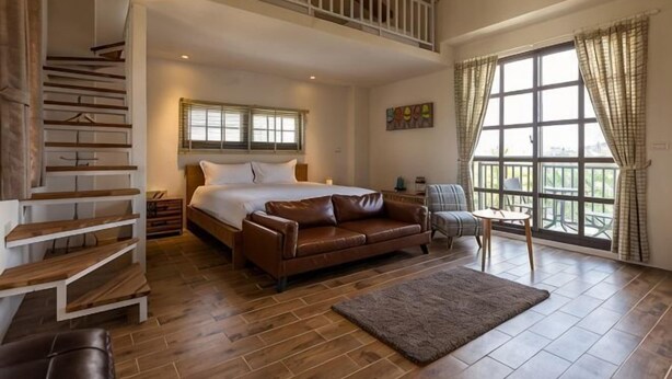 A bedroom with a bed, a brown leather sofa, a wooden staircase, and a large window with curtains. - Forest Bed and Breakfast(Pet friendly) (Hualien)