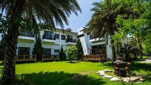 A multi-story hotel with a courtyard featuring a lawn, palm trees, and a decorative fountain. - Forest Bed and Breakfast(Pet friendly) (Hualien)