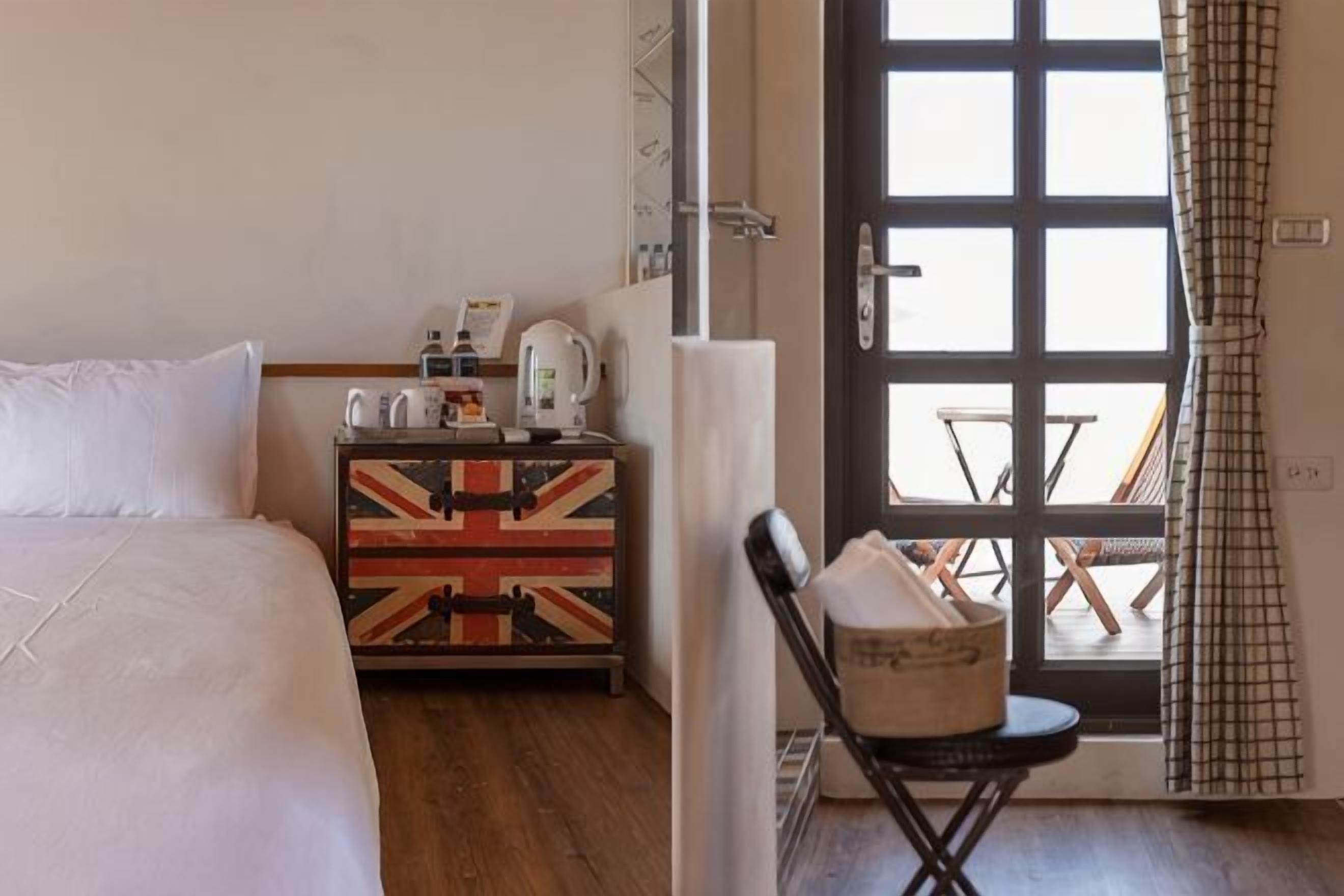 Habitació d'hotel amb un llit, una petita taula de nit amb disseny de la Union Jack, una cadira i vista a través d'una porta.