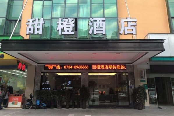 A hotel entrance with a glass facade, a reception desk, and a digital display board. - Sweet Orange Hotel (Hengyang)