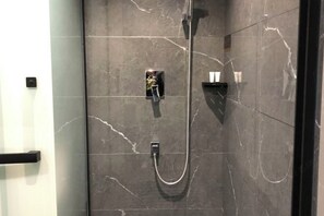 Un baño moderno con ducha envuelta en vidrio, azulejos de mármol y un toallero negro.