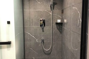Un baño moderno con ducha envuelta en vidrio, azulejos de mármol y un toallero negro.