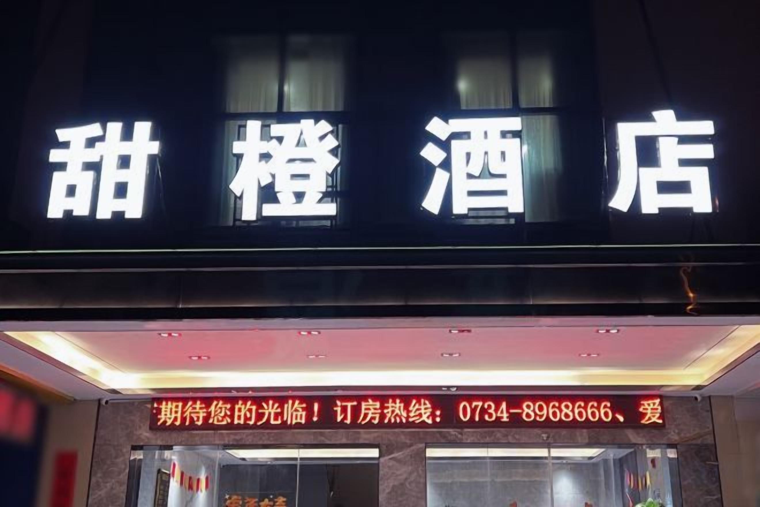 A hotel sign with the name 'Sweet Orange Hotel' and a contact number for inquiries.