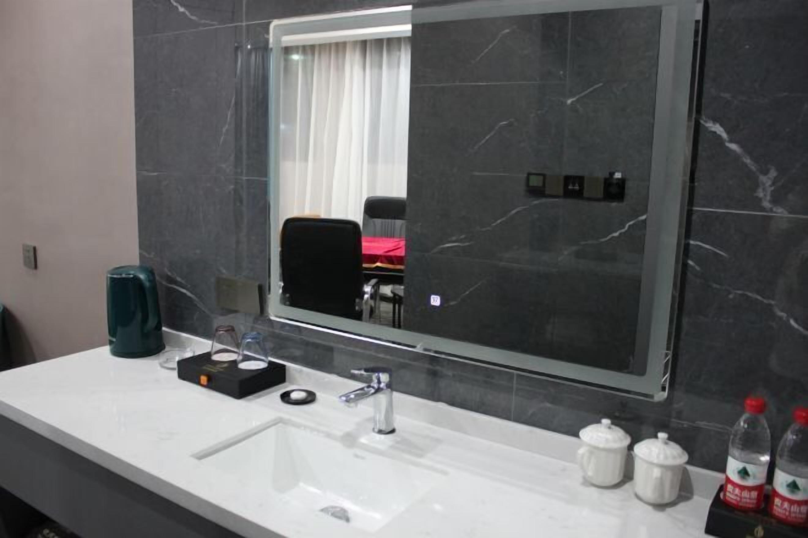 A modern bathroom with a large mirror, a white sink, and a black chair visible in the reflection.