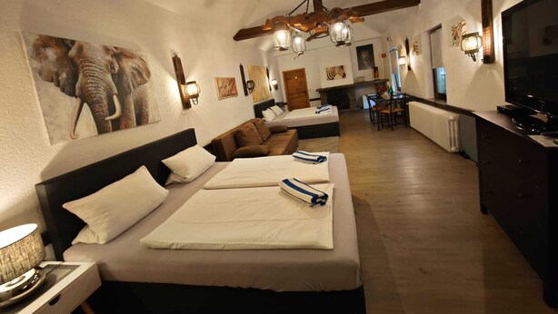 A hotel room with a large bed, a television, a dining area, and artwork on the walls.