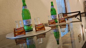 A glass-top table with Ahraqua water bottles, glasses, and packets of hanuta cookies.