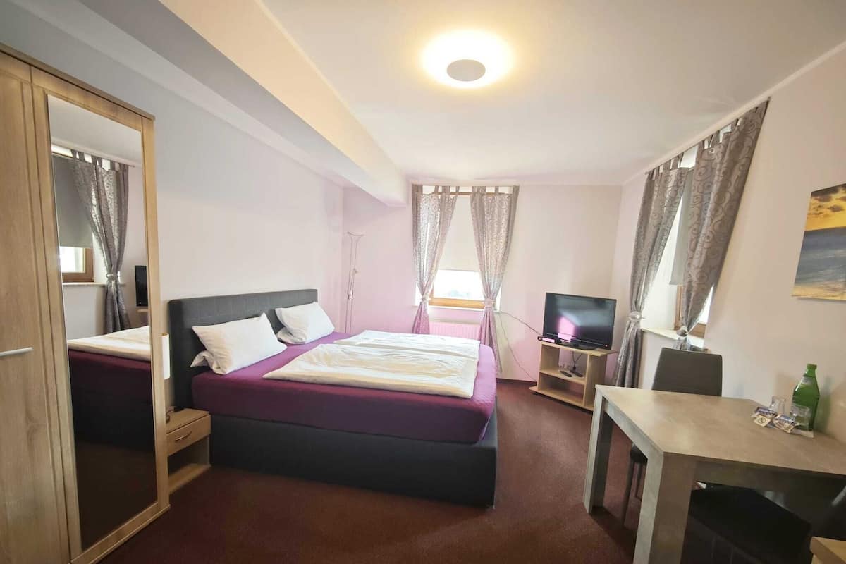 A hotel room with a bed, a desk, a television, and a wardrobe.