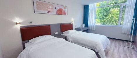 Habitación de hotel con dos camas, una ventana con cortinas, un cuadro en la pared y una mesita de noche.