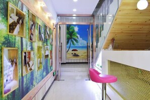 A hallway with framed pictures on the walls, a pink chair, and a beach mural in the background. - Shijiazhuang Yiyou Express Hotel (Youyi South Street Hebei Province Letters and Calls Bureau Branch) (Shijiazhuang)