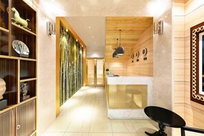A hotel lobby with a reception desk, a wooden reception area, and a hallway with shelves.