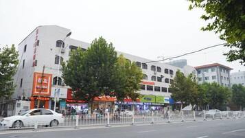 A street view with buildings, a tree-lined sidewalk, and a pedestrian crossing.