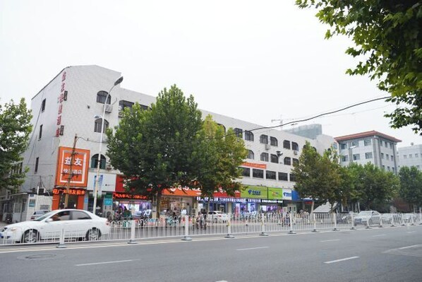 A street view with buildings, a tree-lined sidewalk, and a pedestrian crossing.