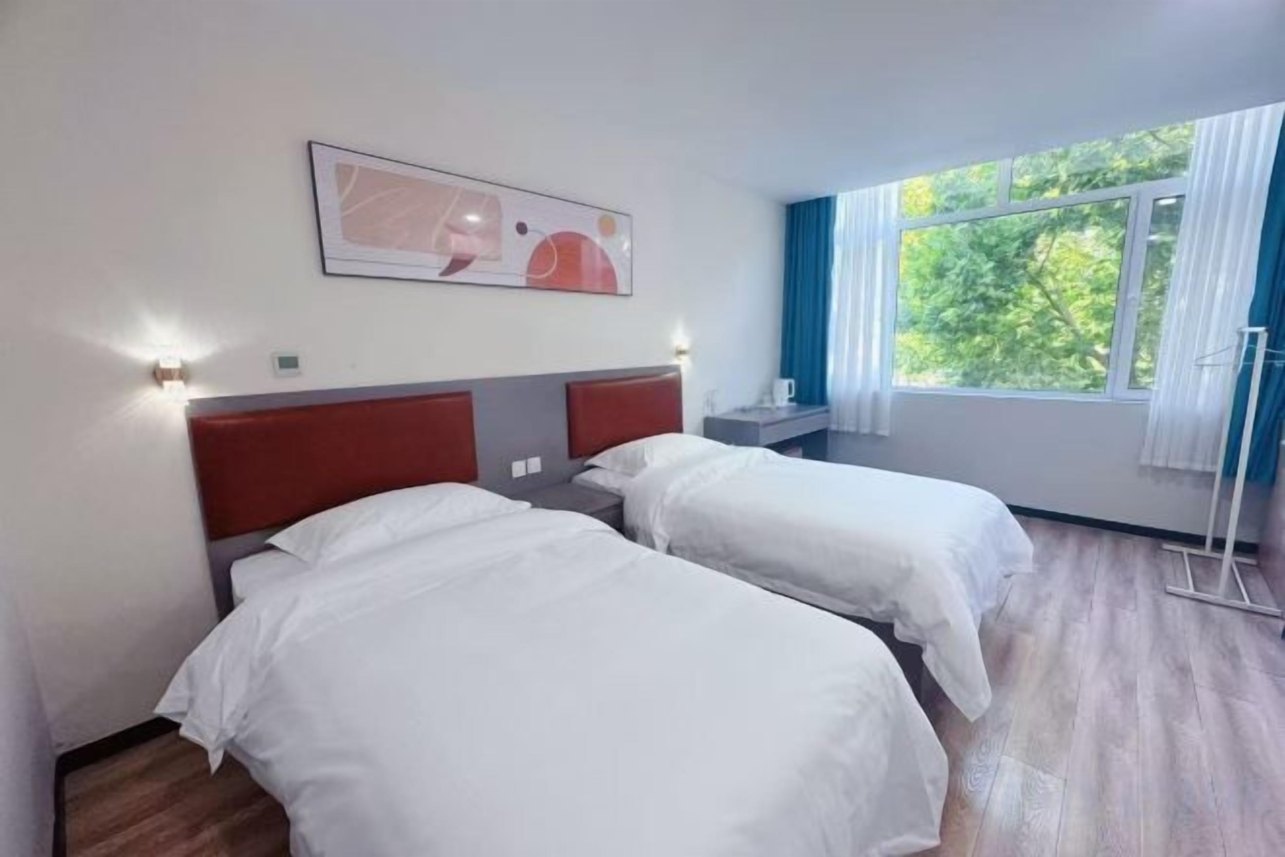 Une chambre d’hôtel avec deux lits, une fenêtre avec des rideaux et un tableau au mur.