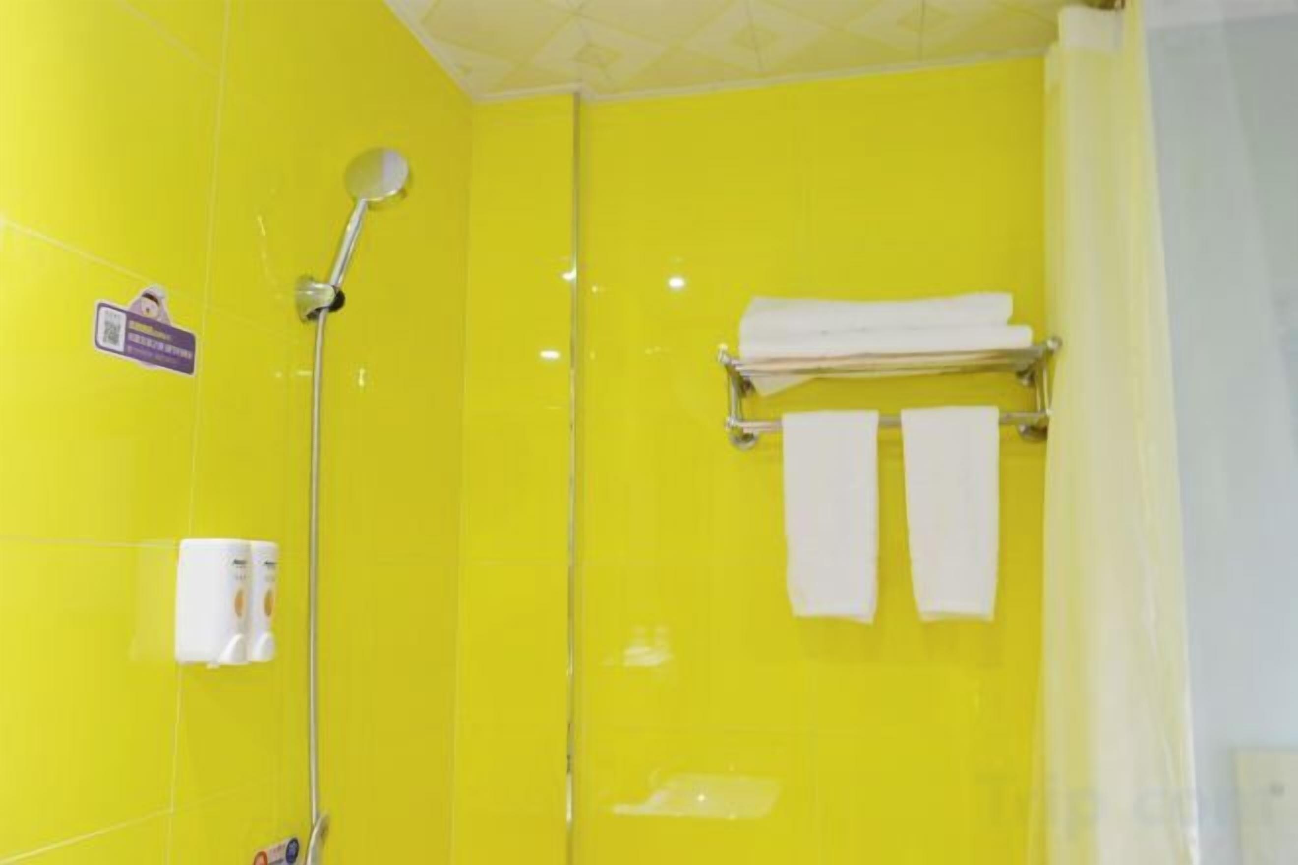 A bathroom with a yellow wall, a shower, and a towel rack with two towels.