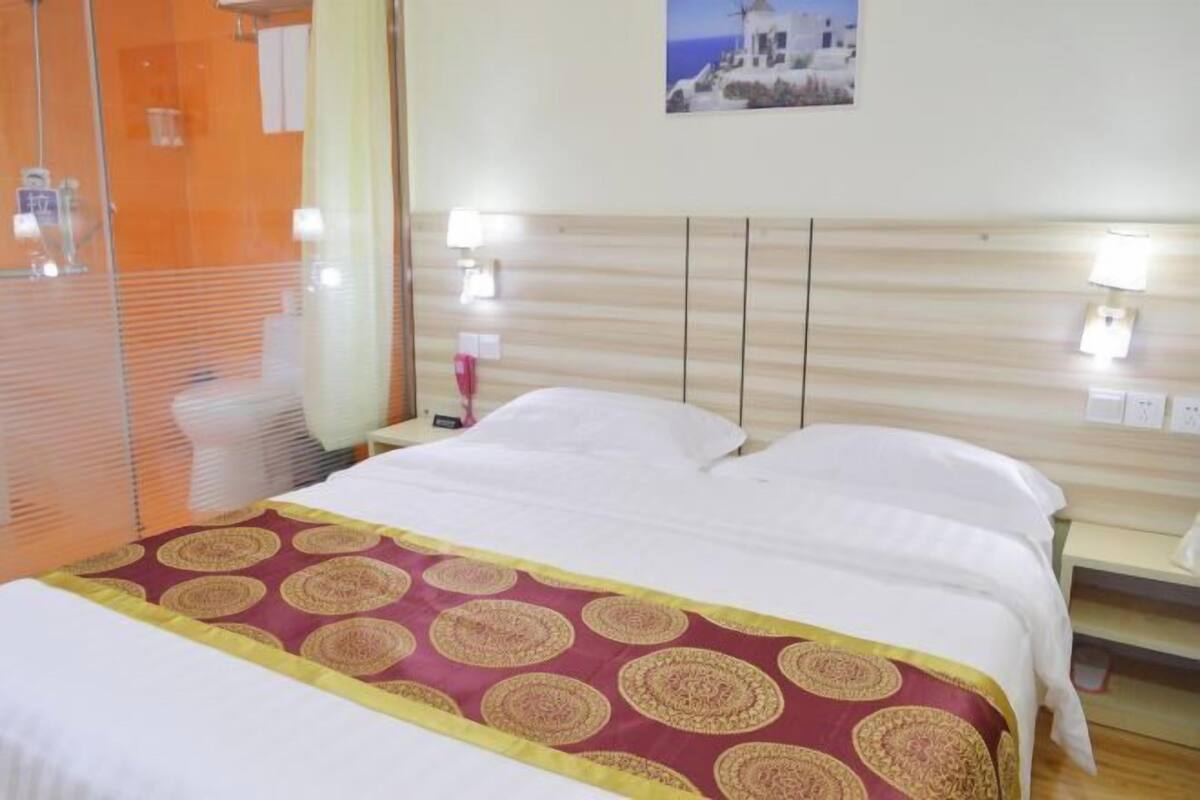 Quarto de hotel com cama, mesa de cabeceira, abajur e quadro na parede.