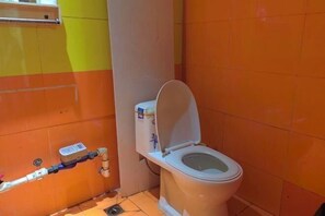Un baño pequeño con inodoro, secador de manos y una tubería a lo largo de la pared.