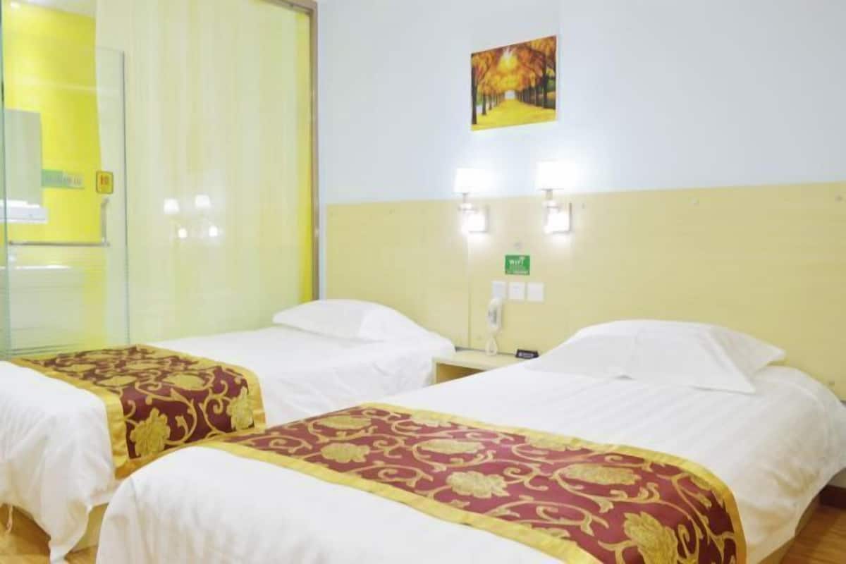 Quarto de hotel com duas camas, cada uma com colcha vermelha e dourada, roupa de cama branca e uma mesinha de cabeceira com abajur.