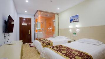 Habitación de hotel con dos camas, un escritorio, un televisor y un baño visible a través de una puerta de vidrio.