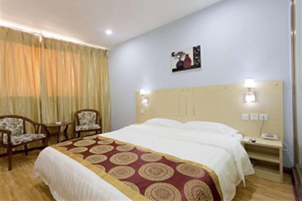 Quarto de hotel com uma cama, duas cadeiras, uma mesinha de cabeceira e um quadro na parede.