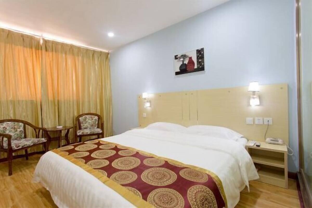 Quarto de hotel com cama, duas cadeiras, mesa de cabeceira e um quadro na parede.