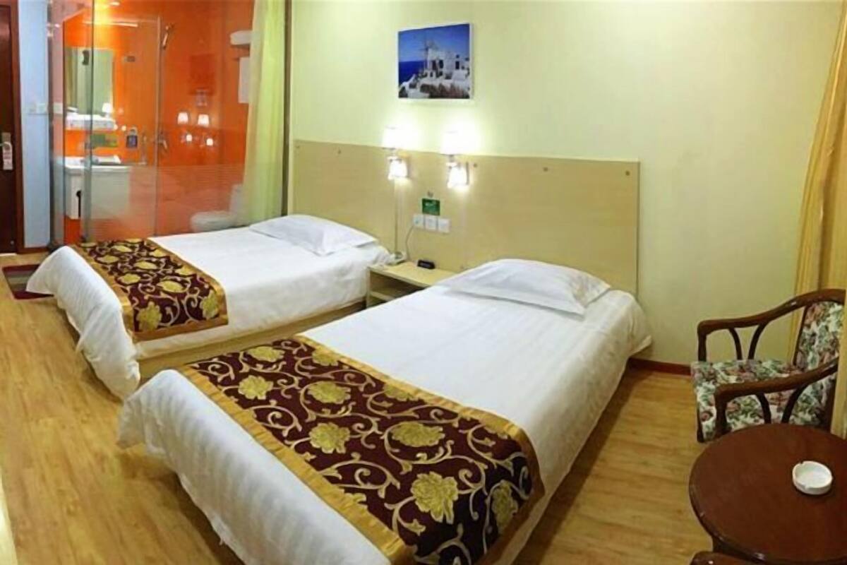 Quarto de hotel com duas camas, uma mesinha, uma cadeira e área de chuveiro.