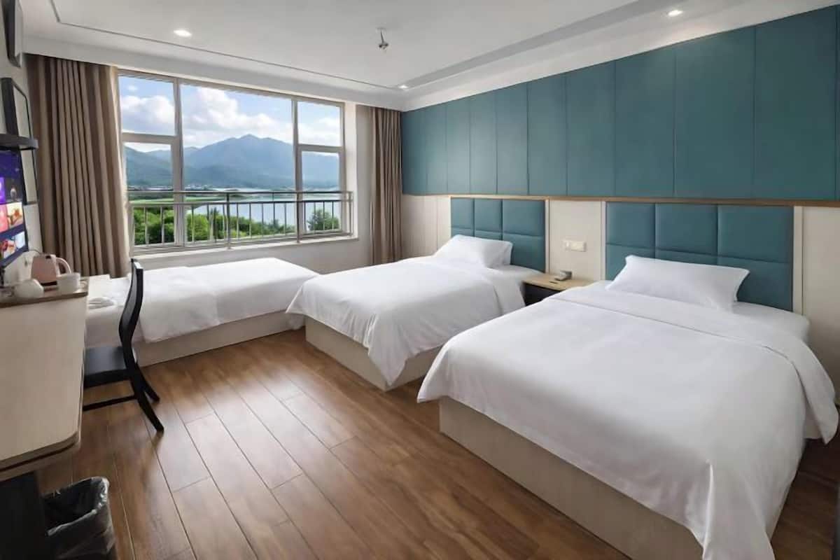 A hotel room with two beds, a desk, a chair, and a view of mountains through large windows.